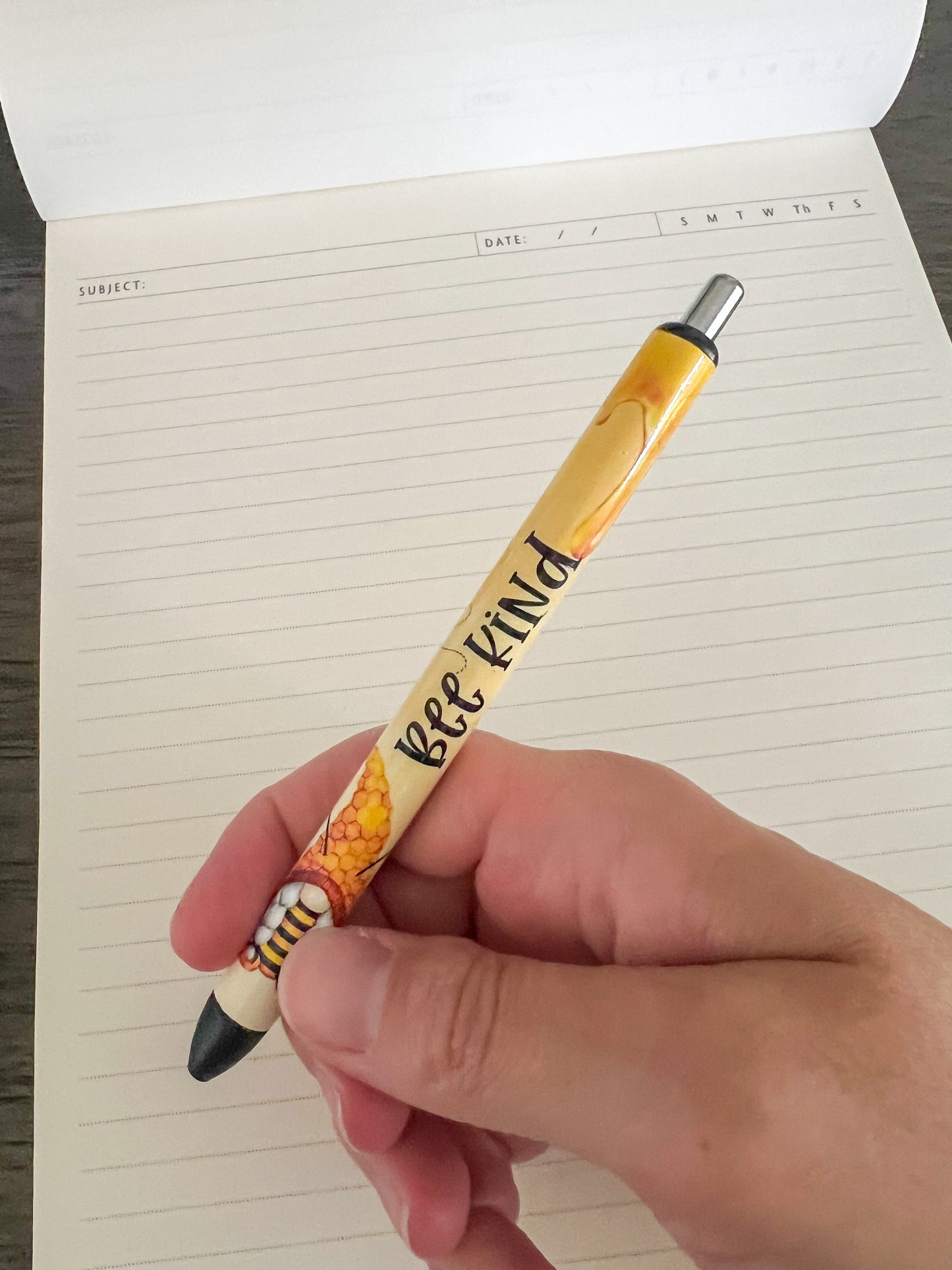 Bee kind pen being held with notebook in background 